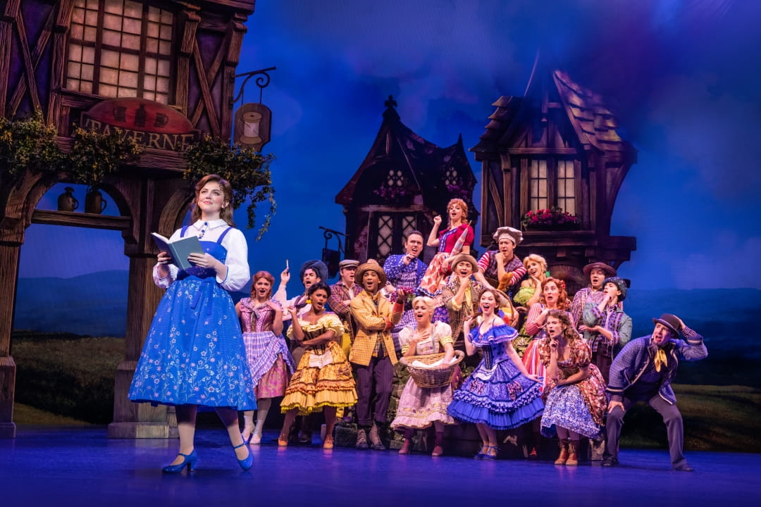 Company cast members in costume on stage excitedly listening to Kyra Belle Johnson. Disney's Beauty And The Beast. Photo By Matthew Murphy. 
